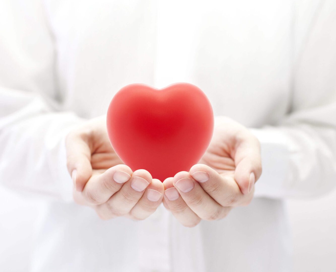 Hands gently holding a red heart symbol.