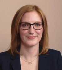 Professional woman with glasses and red hair smiling gently.